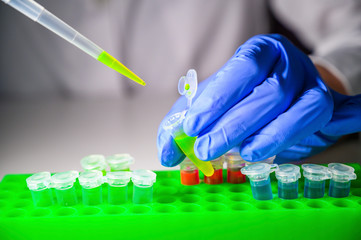 Scientist taking out green solution in eppendorf tube and pipette for biomedical research with tube...