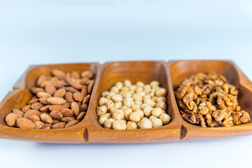 Close-up of healthy raw snack of nuts served in a wooden container, isolated on white background. Raw almonds, raw hazelnuts, raw walnuts.