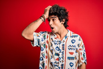 Young handsome man on vacation wearing summer shirt over isolated red background surprised with hand on head for mistake, remember error. Forgot, bad memory concept.