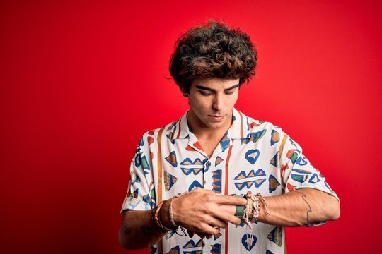 Young handsome man on vacation wearing summer shirt over isolated red background Checking the time on wrist watch, relaxed and confident