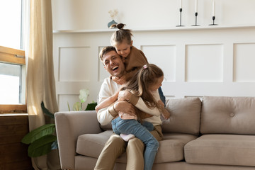 Little girls hug smiling dad playing at home