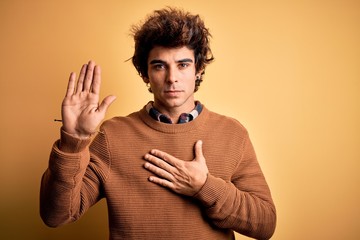 Young handsome man wearing casual shirt and sweater over isolated yellow background Swearing with...