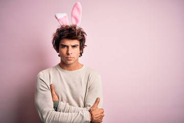 Young handsome man holding easter rabbit ears standing over isolated pink background skeptic and...