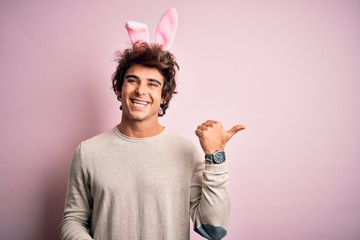 Young handsome man holding easter rabbit ears standing over isolated pink background smiling with...