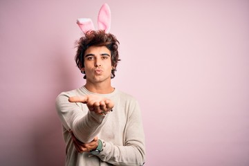 Young handsome man holding easter rabbit ears standing over isolated pink background looking at the...