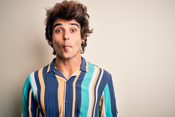 Young man on vacation wearing summer colorful shirt standing over isolated white background making fish face with lips, crazy and comical gesture. Funny expression.