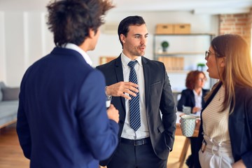 Young beautiful group of business workers working together. Relaxing moment drinking coffee and speaking standing at the office