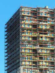 Construction of a high multi-storey building. Skyscraper furnished with metal scaffolding. Dangerous work at height. Modern architecture in the arrangement of the city. Urbanization of the environment