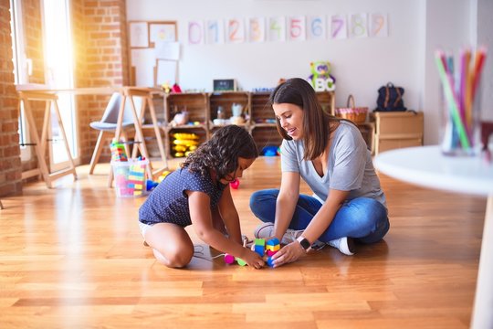 Beautiful teacher and toddler girl playing with train at kindergarten