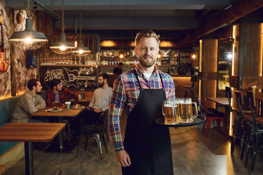 Bearded Waiter With A Tray Of Glasses Of Beer Against The Background Of A Pub Bar