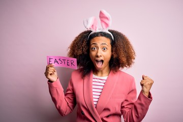 African american woman with afro hair wearing bunny ears holding paper with message screaming proud and celebrating victory and success very excited, cheering emotion