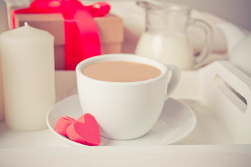 Cup of coffee and a heart shaped red chocolate candies with gift box on the white tray