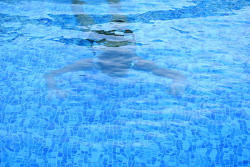 Boy floats under water in the open blue pool in the hotel. To search under water.