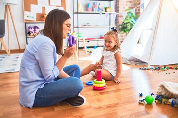 Caucasian girl kid playing and learning at playschool with female teacher. Mother and daughter at playroom playing with inteligence toys