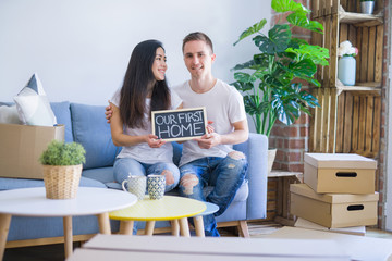 Fototapeta na wymiar Young beautiful couple sitting on the sofa holding blackboard with message at new home around cardboard boxes