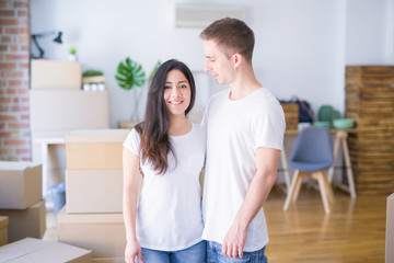 Young beautiful couple standing at new home around cardboard boxes