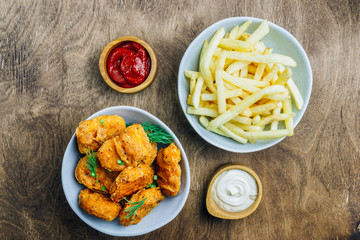 Fried crispy chicken nuggets with french fries and ketchup on wooden background. Top view