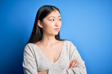 Obraz premium Young beautiful asian woman wearing casual sweater standing over blue isolated background looking to the side with arms crossed convinced and confident