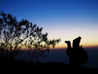 Silhouette of woman photographer at sunrise sky in winter.