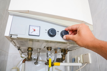 Hands adult men set the temperature of the water in the double-circuit gas boiler.