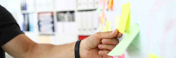 Male arm tearing away sticky paper note from whiteboard closeup