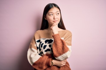 Young beautiful asian woman wearing animal print fashion sweater over pink isolated background with hand on chin thinking about question, pensive expression. Smiling with thoughtful face. Doubt