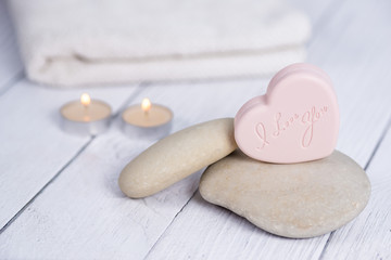 Obraz na płótnie Canvas The concept of a Spa on Valentine's Day. Candles, soap in the form of a heart with the text I love you, stones and a white towel on a wooden background. Relaxation and wellness care. Bath procedure.