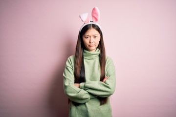 Young asian woman wearing cute easter bunny ears over pink background skeptic and nervous, disapproving expression on face with crossed arms. Negative person.