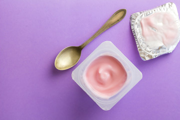 Healthy strawberry fruit flavored yoghurt with natural coloring in plastic cup isolated on purple background with small spoon and foil lid