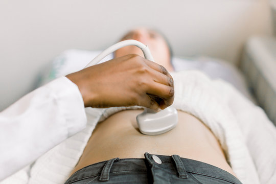 Cropped image of female African doctor hand moving ultrasound transducer on woman's stomach.