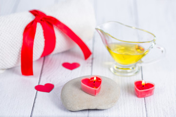The concept of a Spa on Valentine's Day. Red heart-shaped candles, stones, massage oil and a white towel on a wooden background. Relaxation and wellness care. Bath procedure.