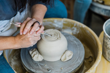 a caucasian woman trimming the base of an unfinished clay pot on a pottery wheel close up and adding detail work to the bottom