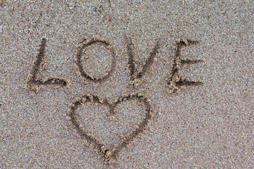 The word love is written with a finger in the sand on a beach. love message written in sand.