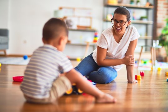 Beautiful teacher and toddler boy playing with tractor and cars at kindergarten