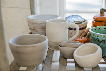 A shelf full of unfinished clay ceramic pottery pieces that are waiting to be fired in a kiln