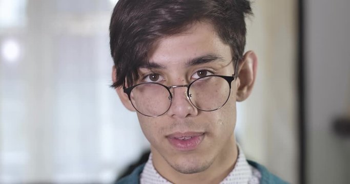 Portrait of handsome confident Caucasian man with brown eyes looking at camera. Close-up of young brunette guy adjusting eyeglasses. Cinema 4k ProRes HQ.