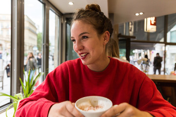 Fototapeta na wymiar Young Woman in Coffee Shop Holding Cappuccino Mug Smiling and Looking Away