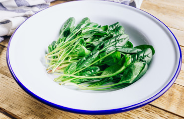 Fresh green baby spinach on plate on wooden rustic table. Healthy diet, vegetarian food concept.