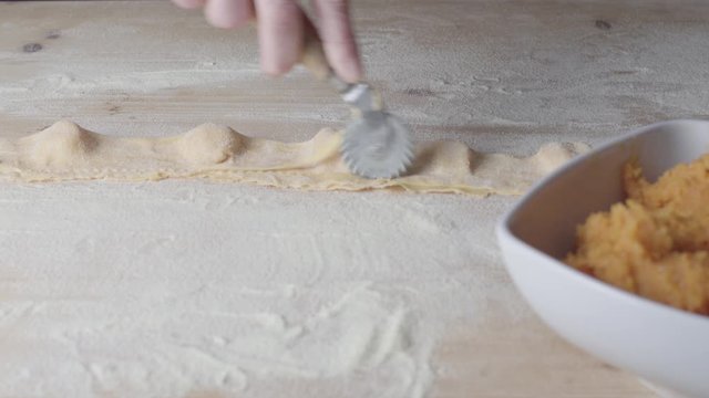 Closeup process making ravioli vegan homemade pasta. Housewife cook cutting with a cutting wheel 'tortelli di zucca', traditional italian pasta, woman cooking food on kitchen