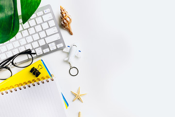 Top view of keyboard, notepad, shells and airplane toy on white table. Travel planning or freelance concept.