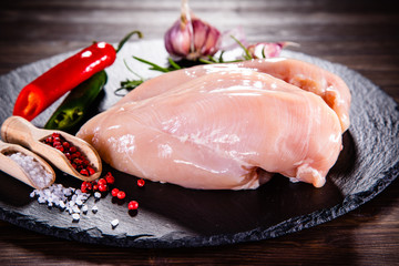 Raw chicken breasts with spices on black stone plate