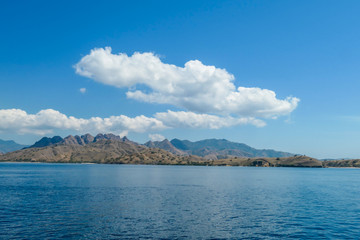 Obraz premium A view on idyllic island in Komodo National Park, Indonesia. There are few clouds above the island. Calm and clear surface of the sea. Island hoping. Perfect day for sailing