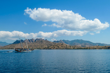 Fototapeta premium A view on idyllic island in Komodo National Park, Indonesia. There are few clouds above the island. Calm and clear surface of the sea. Island hoping. Perfect day for sailing