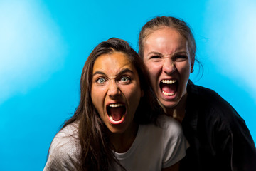 Two Women Looking at Camera and Screaming on Blue Background