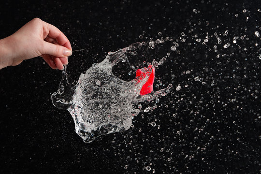 Cropped Hand Of Person Exploding Water Bomb Against Black Background