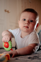 Fototapeta premium The kid is playing a plastic rattle. The boy has his first teeth. The baby lies on his stomach and plays with toys. Little boy is interested.