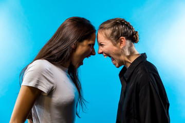 Profile of Two Young Women Shouting at One Another on Blue Background