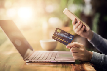 Yong female hand holding plastic credit card and using laptop. Online shopping or paying concept.