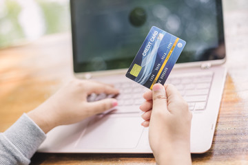 Yong female hand holding plastic credit card and using laptop. Online shopping or paying concept.