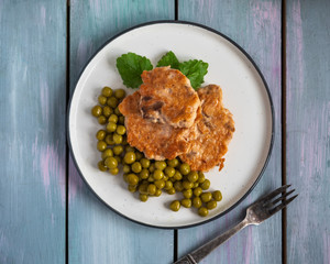 Delicious fish cakes with green peas for a light breakfast of chum salmon fish with canned green peas and sprigs of lemon balm, fork lie on a wooden rustic tray